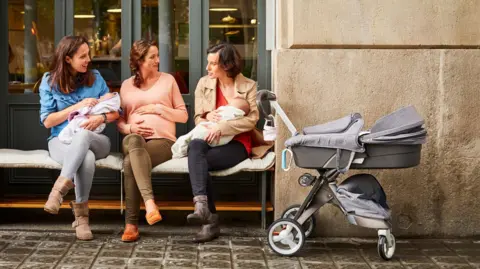 Getty Images Three women sitting together and chatting with their babies and prams