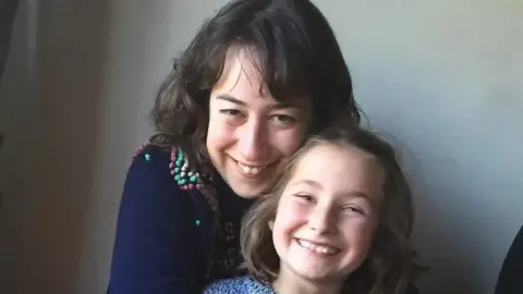 Merope Mills Woman with dark brown hair smiles with little girl with light brown hair, who also smiles.