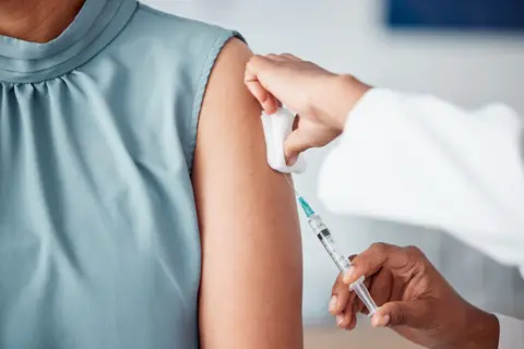 Getty Woman in a blue silk sleeveless job receiving an injection from a medical professional