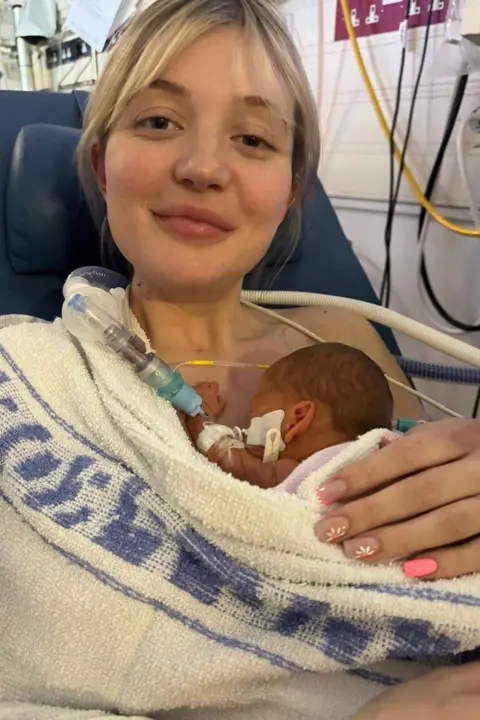 Atlanta Mcintyre A young mother holds her newborn baby, wrapped in a hospital blanket.