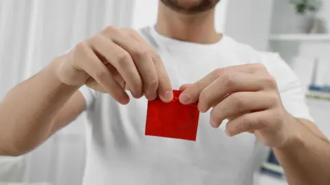 Getty Images Man in a white t-shirt opens a red condom packet
