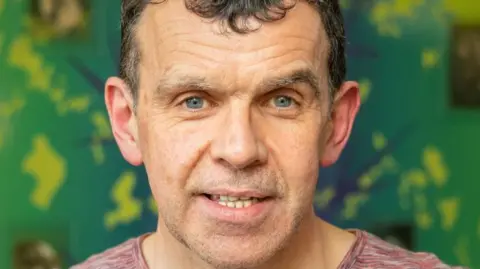 University of Aberdeen Man, Sandy Patience, smiling and looking at camera, against a green background.