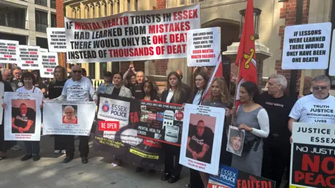 PA Media Bereaved families gather outside the Lampard Inquiry at Arundel House in London. They hold placards and signs calling for action, with many displaying photos of their loved ones.