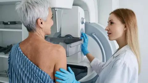 Getty Images A woman goes for a mammogram.  She is pictured alongside a female medical professional. 