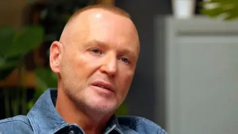 BBC / Twenty Twenty Productions Ltd Owen O'Kane, a therapist, wearing blue denim shirt, against blurred interior background