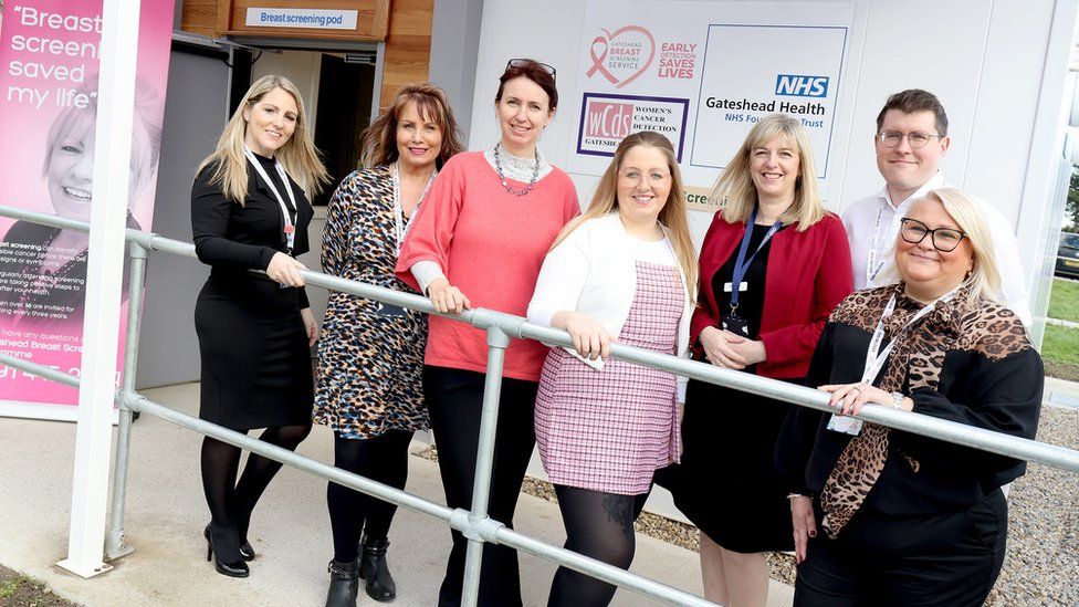 Five women and a man stand outside a small medical looking building