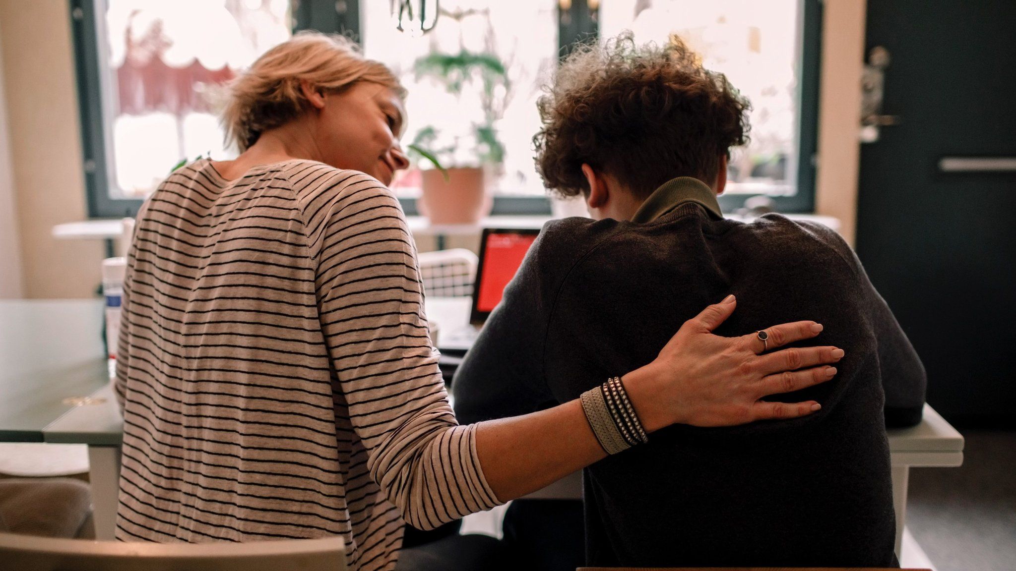 Adult has arm around child comforting them as they do school work