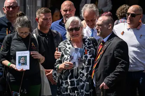 Getty Images Victims and families stand outside Methodist Central Hall in Westminster holding photographs of their loved ones