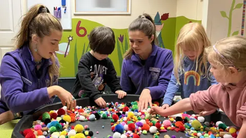 Topaz and Sade Oram playing with children at Leaping Frogs Nursery using different coloured objects 