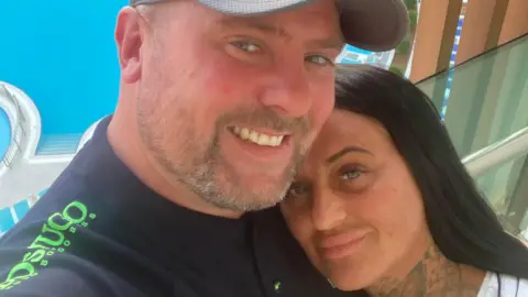 Vicky Boyd A man and woman hugging and smiling at the camera in front of a swimming pool