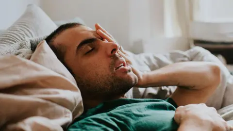 Getty Images Man looking unwell and holding his head in bed