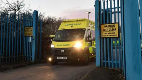 Getty Images Photograph of ambulance being driven through blue gates.