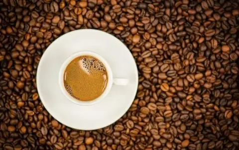 Getty Images A cup of coffee sitting on top of a layer of coffee beans 