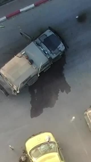 An overhead view of a street shows an explosion beside a vehicle and then a group of people scattering from where smoke begins to emerge.