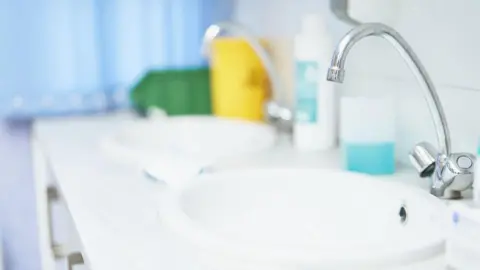 Getty Images A clinical sink with a tap over it, with soap on the side of it 