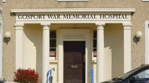 PA Media The front façade of Gosport War Memorial Hospital. It has four white pillars, with the hospital's name in black letters above them.