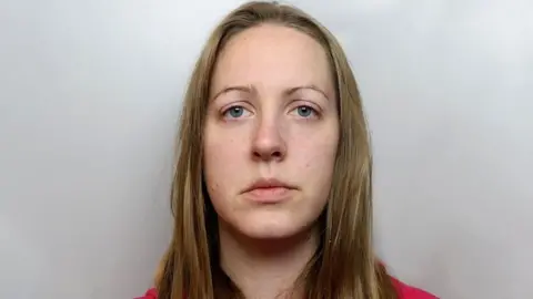 Cheshire Constabulary Lucy Letby police photograph - she is looking straight ahead. She has blond shoulder length hair, and is standing in front of a grey background 