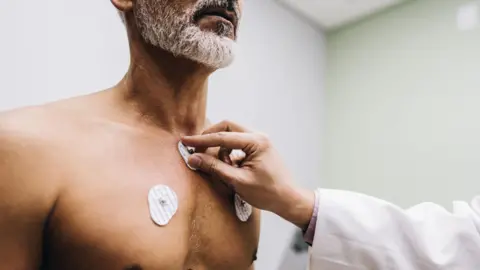 Getty Images A doctor carries out an ECG exam on a patient, placing electrode sensors on the man's chest