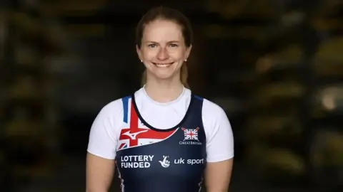 NAOMI BAKER Paralympic rower Erin Kennedy poses for a photo in her Team GB rowing uniform. She is smiling, has long brown hair and small pearl earrings