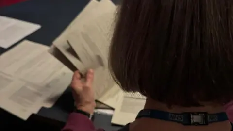 A doctor photographed from behind. She has brown hair and is looking at some paperwork