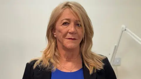 Michelle Drage, a woman with long blonde hair wearing a black jacket and a blue top