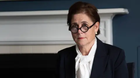 PA Media Baroness Lampard sits in the inquiry office at Arundel House in London. She is wearing a white shirt and navy suit. Her glasses are rounded and tortoiseshell in colour and she is looking direct at the camera with her hair up. She is wearing pearl earrings and is sitting in front of an information folder