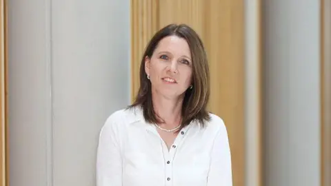 Nottingham Trent University Dr Emma Ireton from Nottingham Trent University looking at the camera. She has shoulder length brown hair and blue eyes. She is wearing a long sleeved, while shirt and a white necklace.