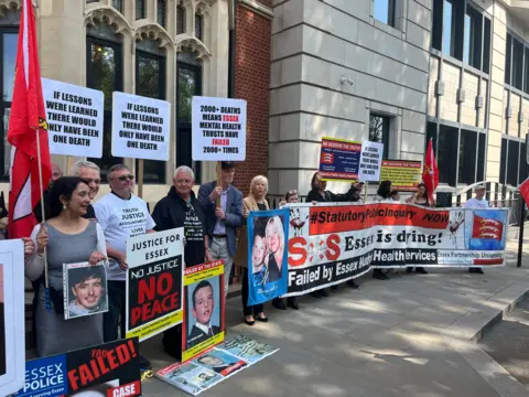 RICHARD DANIEL/BBC Families standing outside Arundel House in London where the public inquiry is entering its next phase. There are about 12 people pictures who are holding placards and posters and flags calling for justice. One reads 'If lessons had been learned, there would have only been one death.