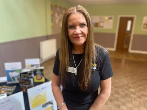 Lynda Leadbetter in a church hall, brown hair and wearing a navy blue T-shirt. standing in front of a stand about her weight loss group.