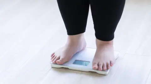 Getty Images A child stands on weighing scales wearing black leggings and bare feet