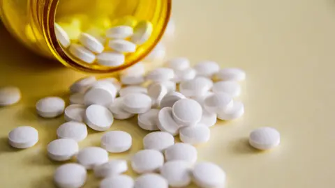 Getty Images A yellow bottle spilling out white circular pills onto a surface