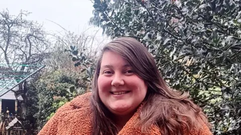 Sharon Johnstone, smiling at camera. She is standing in a garden, wearing a fluffy coat.