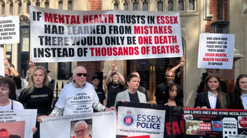 PA Media A large group of people holding placards outside the Lampard Inquiry in London. Their placards criticise mental health trusts in Essex and call for action.