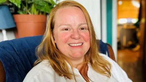 BBC Woman, Marlene Lowe, with blonde hair, and white blouse, smiling at camera.