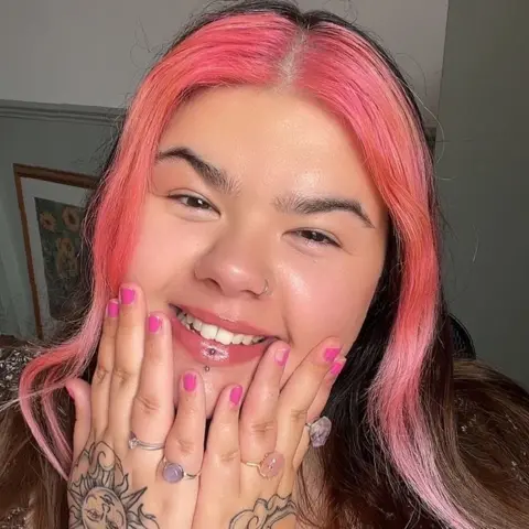 Kayleigh Watson Kayleigh Webster smiling at the camera with a bright pink streak in her hair