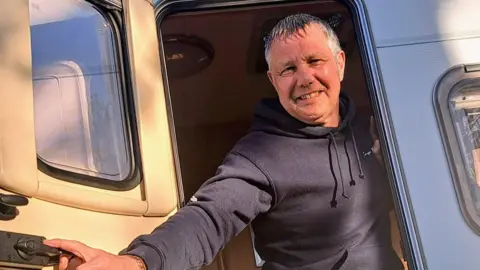 Family handout Jabez Petherick, smiling whilst wearing a blue-grey hoodie and opening a caravan door