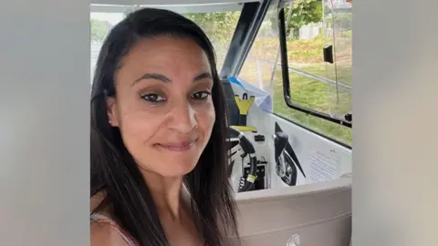 Syreeta Sandhu Syreeta Sandhu smiles at the camera. She is in the driver's seat of a car