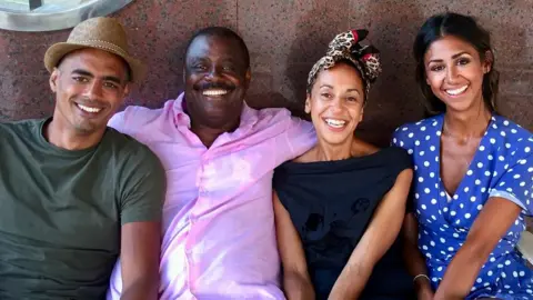 Handout Mel Tottoh with his three children, a son and two daughters, all grown up, smiling and wearing casual clothes as they sit beside their father who is wearing a pink shirt