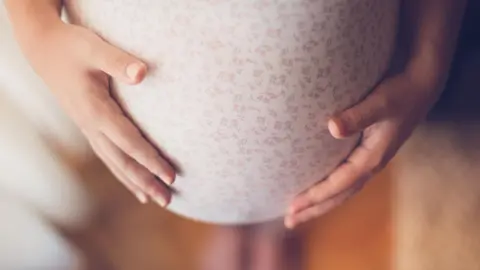 Getty Images Looking down on a woman's heavily pregnant tummy, with both hands on either side of it 