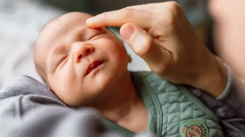 Getty Images A newborn baby with eyes closed and mum gently stroking baby's forehead with a finger.