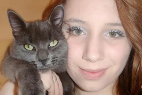 Figueiredo family Alice, a woman with long blonde hair, poses for a photo while holding a grey cat