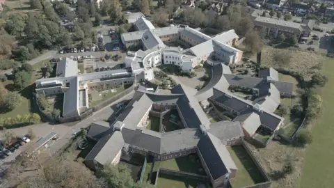 An aerial view of Goodmayes Hospital, Ilford, showing many white and grey rectangular buildings forming a near circle