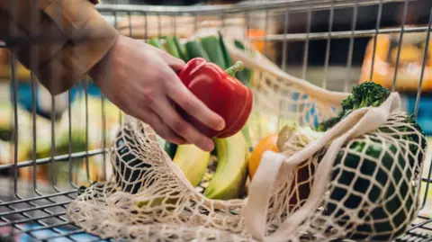 Getty Images Close-up shot of female hand putting a red bell pepper into a mesh grocery bag.