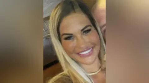 Gemma Gray Gemma Gray, woman in her 40s, is smiling at the camera. She has blonde hair. She has very straight white teeth, shaped eyebrows and large lips with a pink gloss on them, she's wearing a gold necklace and is tanned. 