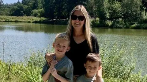 Rachel Williams Rachel Williams, who has long blonde hair, stands with her arms around her two sons, who have fair hair. They are standing in front of a river in the sunshine with trees in the background