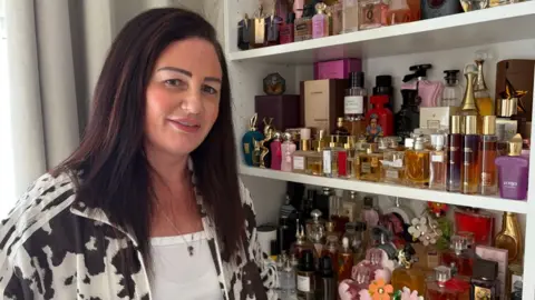 A woman with long dark brown hair wearing a cow print jacket standing in front of a display of perfumes 