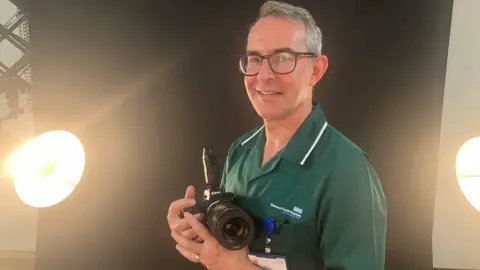 Jason Randall a medical photographer holding a digital camera used to photograph skin lesions. He is pictured in the special studio set up for patients at Nottinghamshire's King's Mill hospital