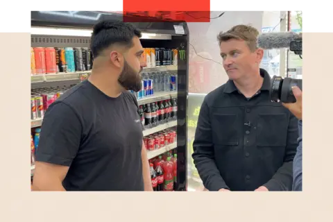 BBC/Phillip Edwards Ed Thomas speaks to a corner shop assistant 