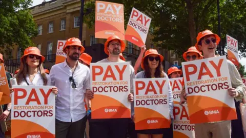 Getty Images Resident doctors, also known as junior doctors, hold placards in support of fair pay during a demonstration in Whitehall outside Downing Street as they begin their latest strike over pay, July 2025. 