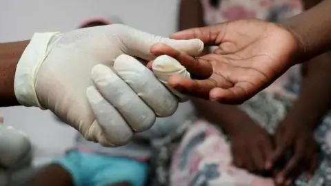 Reuters A glove-wearing nurse takes a blood sample from a child for an HIV test while the child's mother looks on at a clinic in Diepsloot, north of Johannesburg, South Africa, 12 March2025